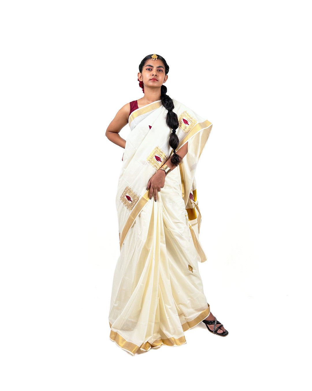 Woman wearing a white kasavu saree with gold border and red leaf embroidery on a white background