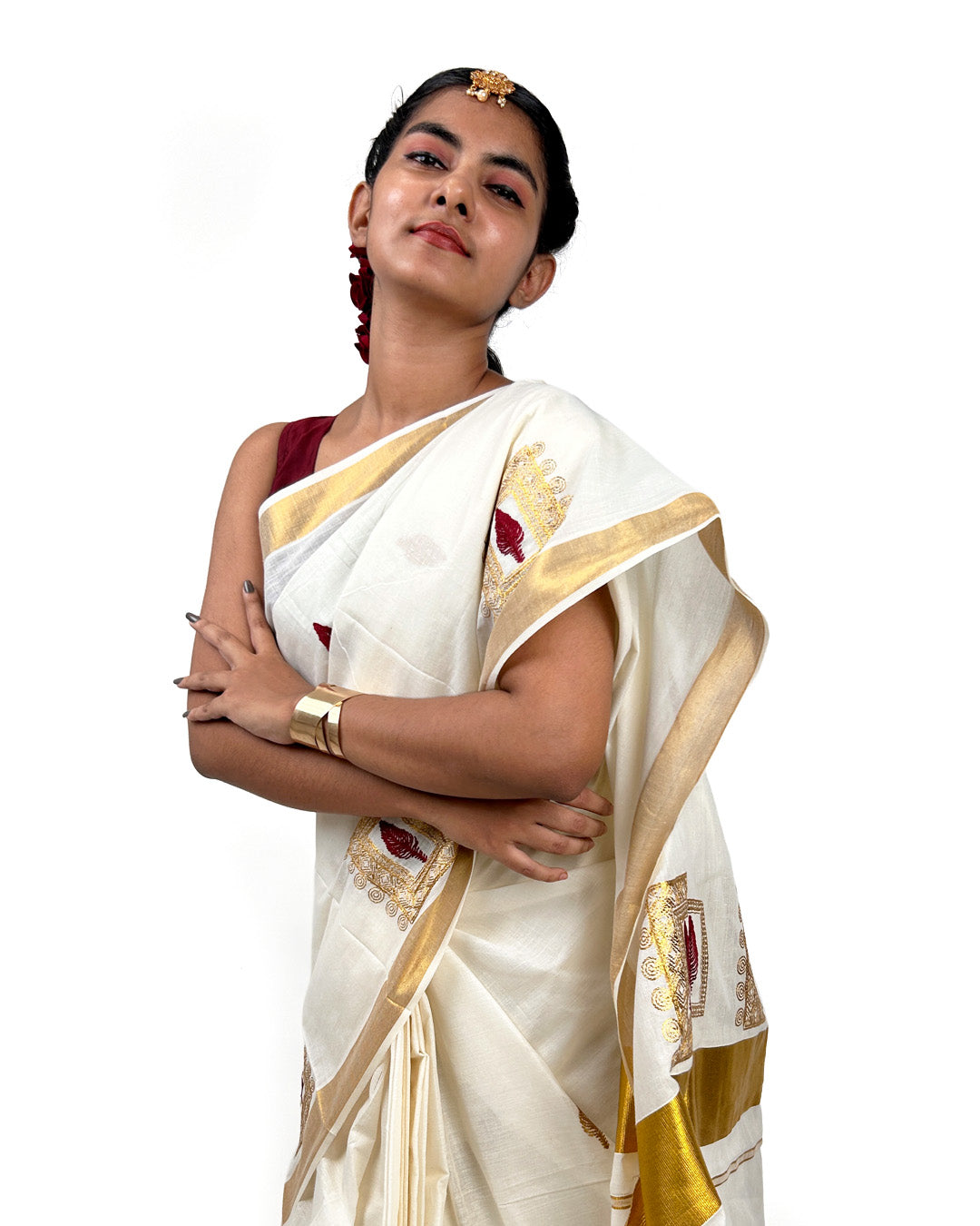 Woman wearing a white kerala saree with gold and red emroidered leaf motif on a white background