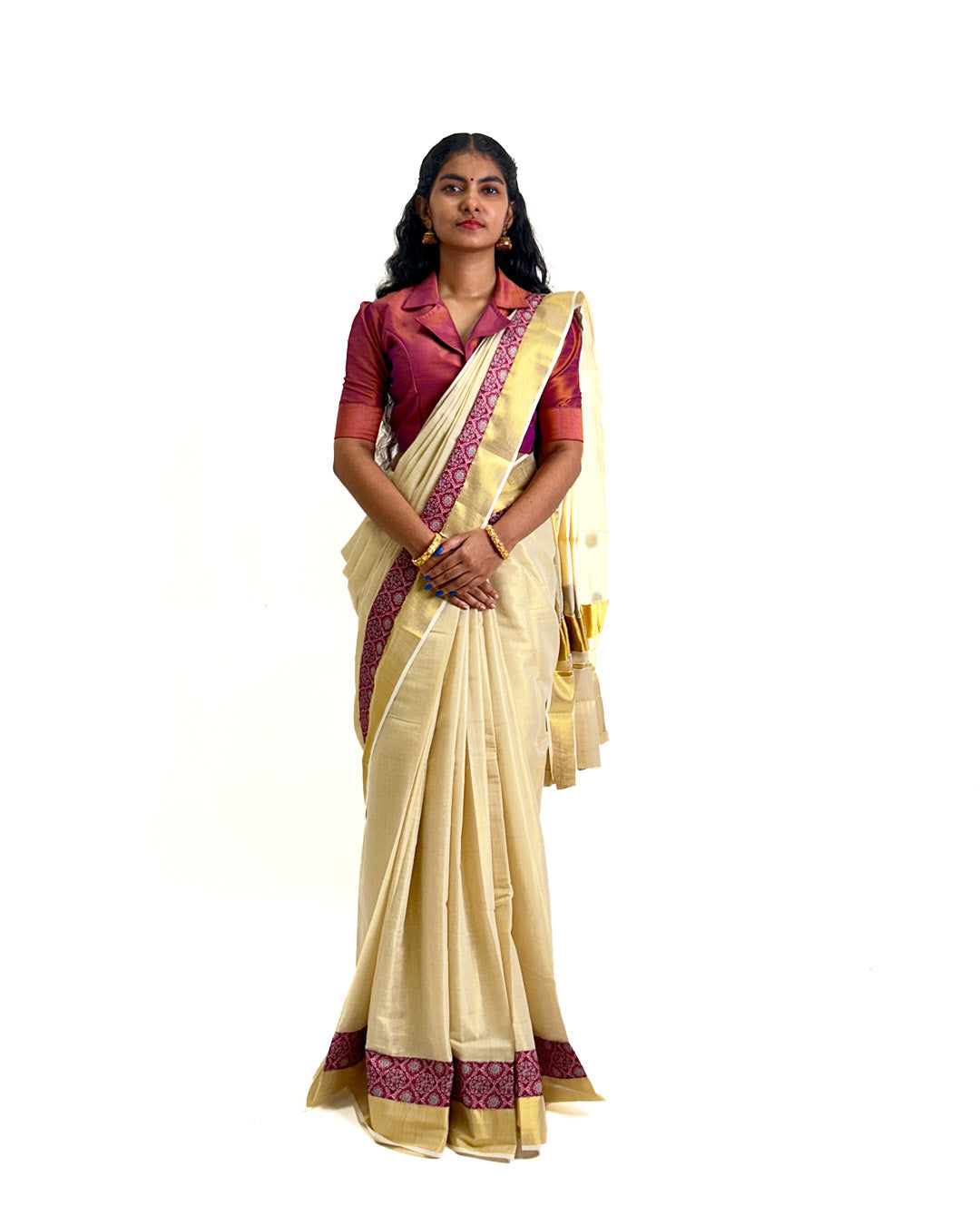 Woman wearing a traditional Kerala kasavu saree with maroon border, styled with a maroon blouse — photographed on a white background. Perfect for Onam, weddings, and festive occasions.