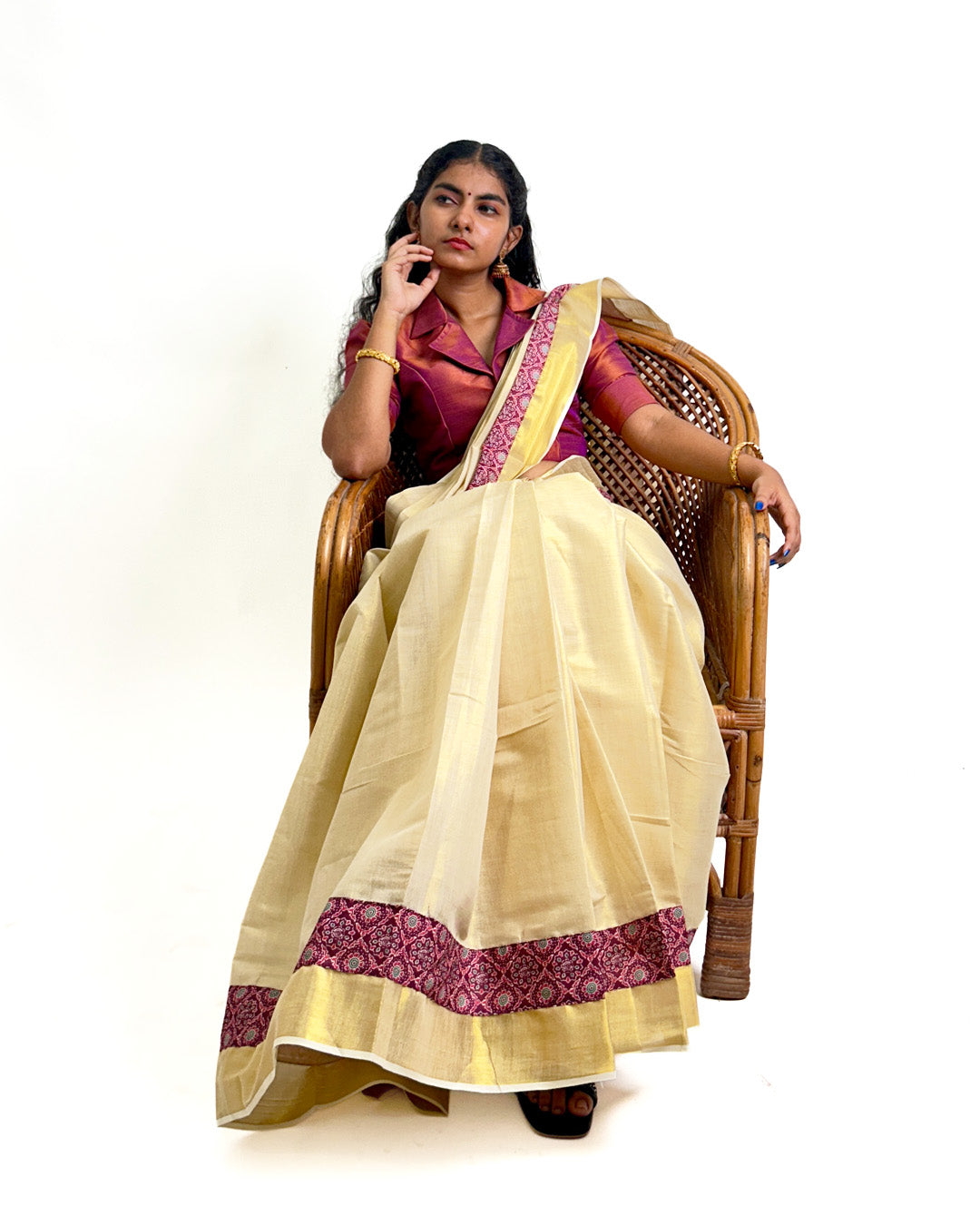 Woman wearing a traditional Kerala kasavu saree with maroon border, styled with a maroon blouse — photographed on a white background. Perfect for Onam, weddings, and festive occasions.